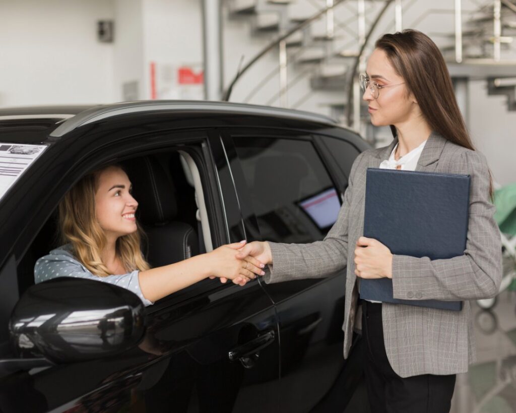  A smiling woman in a car shakes hands with a title pawn representative, symbolizing the easy and fast approval process for title pawns available to Ariton, AL residents at Panhandle Title.