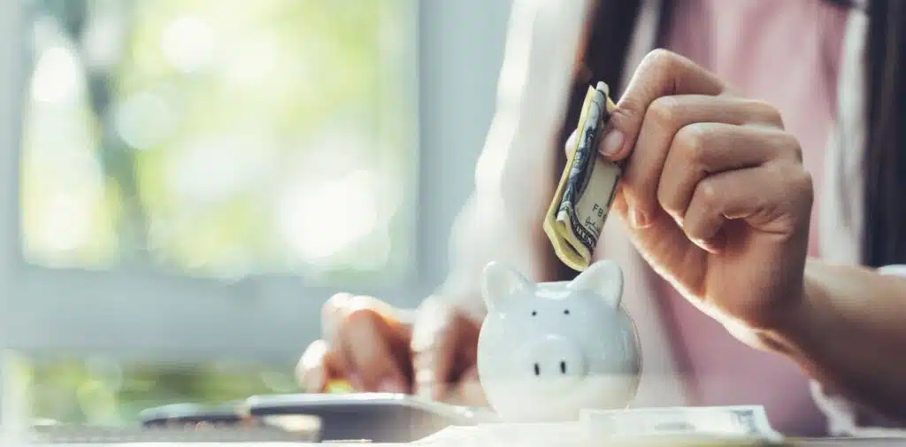 Two people shake hands while simultaneously exchanging a bundle of $100 bills over a desk with documents