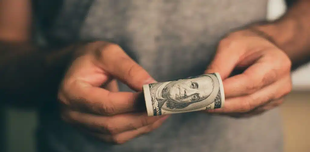 Four hands raised against a light blue background holding cash, a house model, a credit card, and a calculator