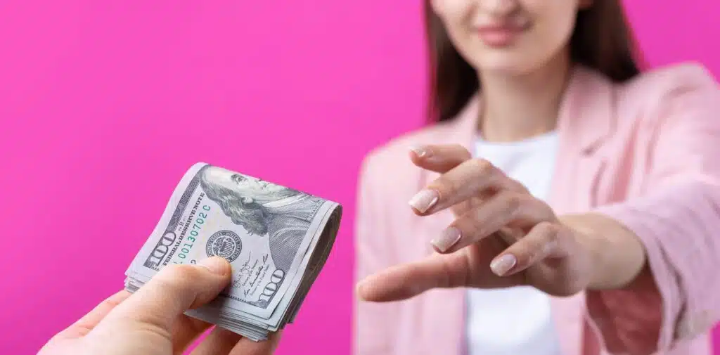 Close-up of two hands holding a tightly rolled $100 bill featuring Benjamin Franklin's portrait