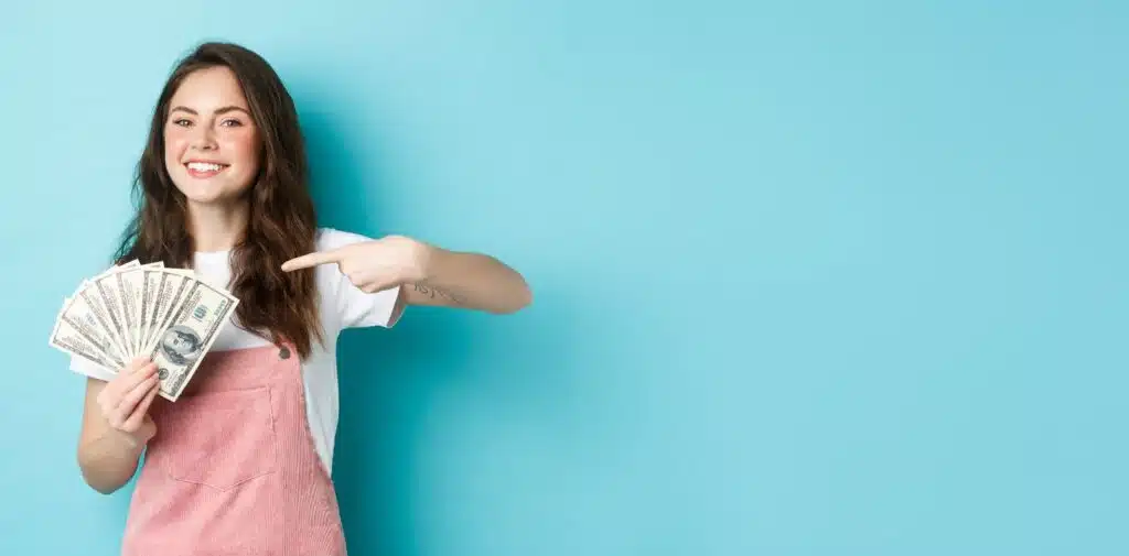 A woman in a plaid shirt holds up a dollar bill near a desktop computer with more bills spread on the keyboard