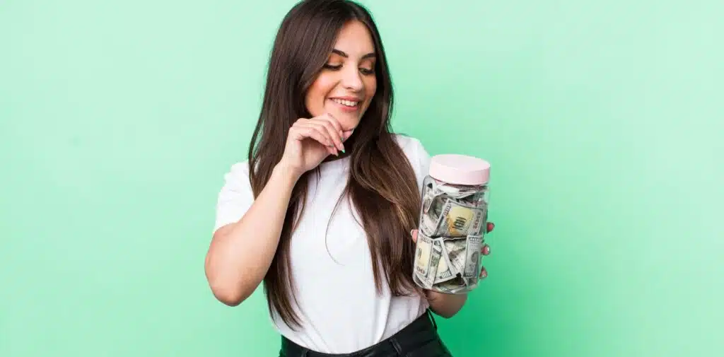 A hand in a blue suit holds three fanned-out US dollar bills including a $10 and $5 against a warm background