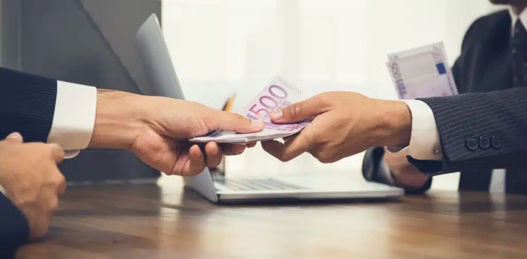 Two people exchange a stack of $100 bills over a signed contract document with a justice scale visible nearby