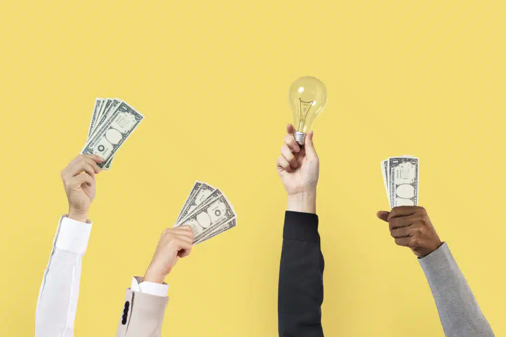 Several hands holding one-dollar bills and a light bulb against a yellow background.