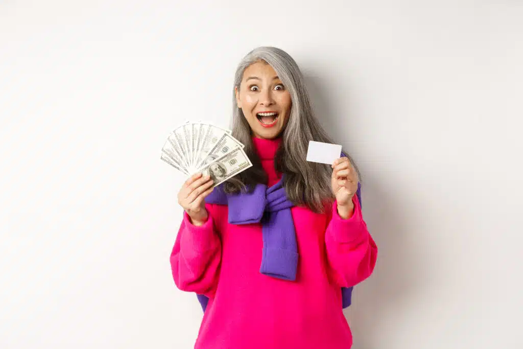 Smiling older woman holding bills and a card against a light background.